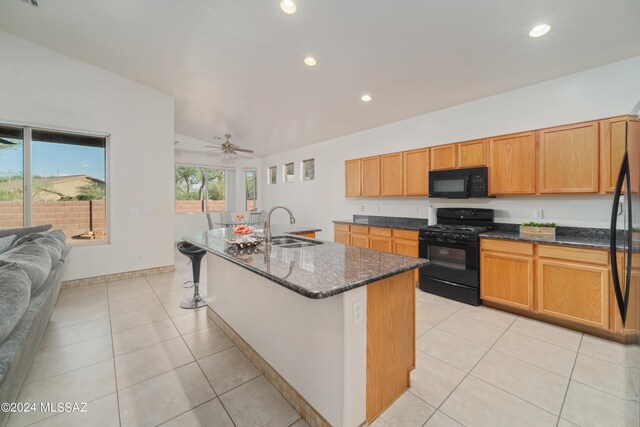 kitchen with a kitchen island with sink, sink, black appliances, dark stone countertops, and ceiling fan