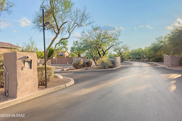 view of road featuring a gate, curbs, a gated entry, and street lights