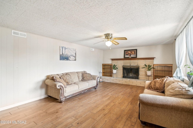 living room featuring light wood finished floors, a brick fireplace, baseboards, visible vents, and ceiling fan