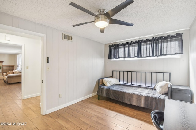 bedroom featuring a textured ceiling, visible vents, a ceiling fan, and wood finished floors