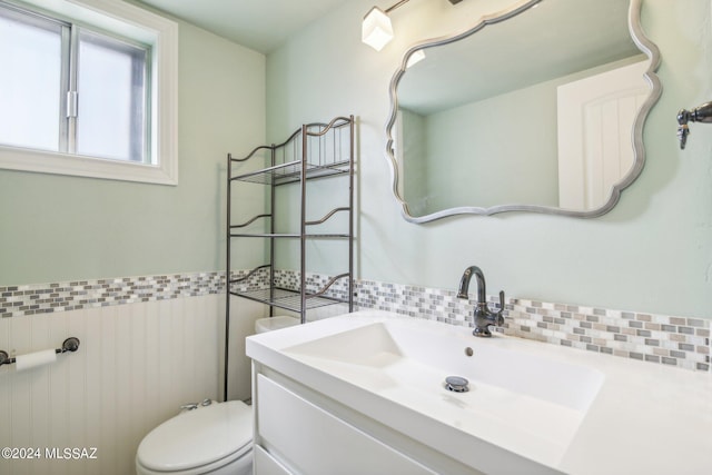 half bath with tile walls, a wainscoted wall, toilet, and vanity
