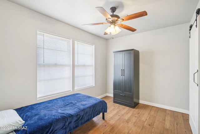 bedroom featuring baseboards, a barn door, light wood-style flooring, and ceiling fan