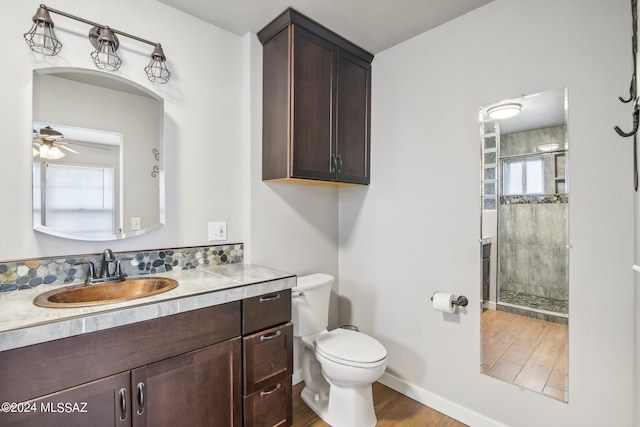 bathroom featuring vanity, toilet, baseboards, ceiling fan, and tiled shower