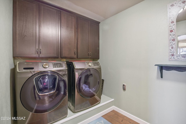 clothes washing area featuring cabinet space, baseboards, washer and dryer, and wood finished floors