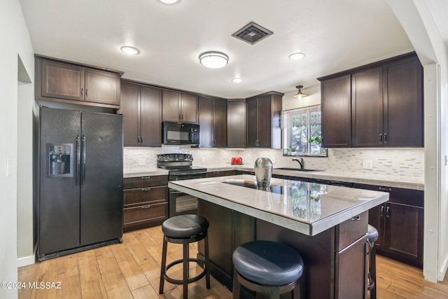 kitchen with dark brown cabinetry, a sink, a breakfast bar, visible vents, and black appliances
