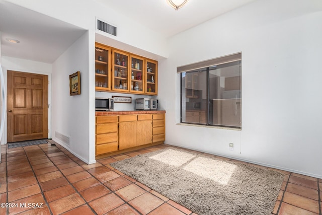 kitchen featuring stainless steel microwave, glass insert cabinets, visible vents, and baseboards