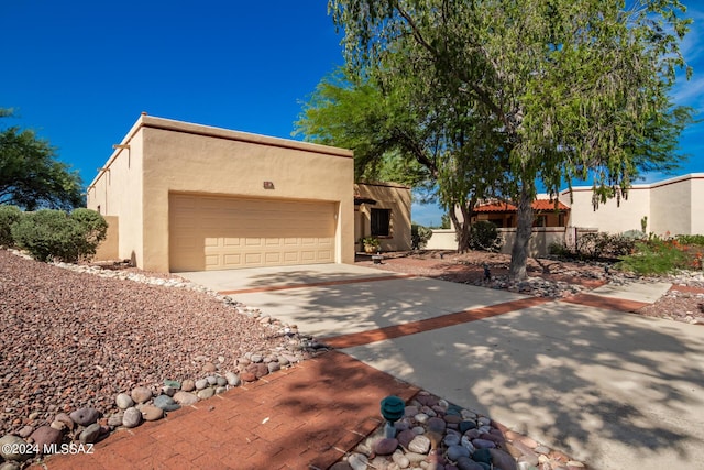 pueblo revival-style home with driveway, an attached garage, and stucco siding