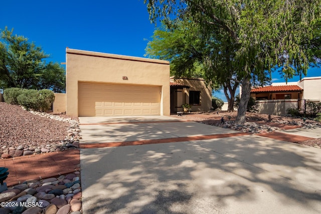 pueblo revival-style home with a garage, concrete driveway, fence, and stucco siding