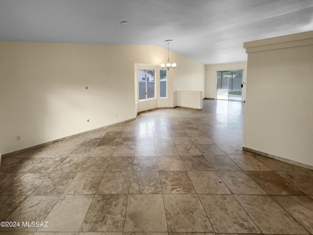 empty room featuring a chandelier, vaulted ceiling, and baseboards