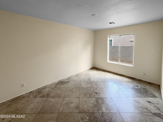 spare room featuring a textured ceiling, visible vents, and baseboards