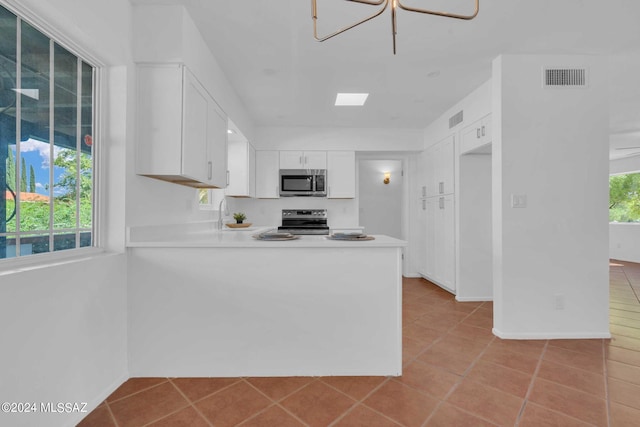 kitchen with visible vents, a peninsula, stainless steel appliances, light countertops, and white cabinets