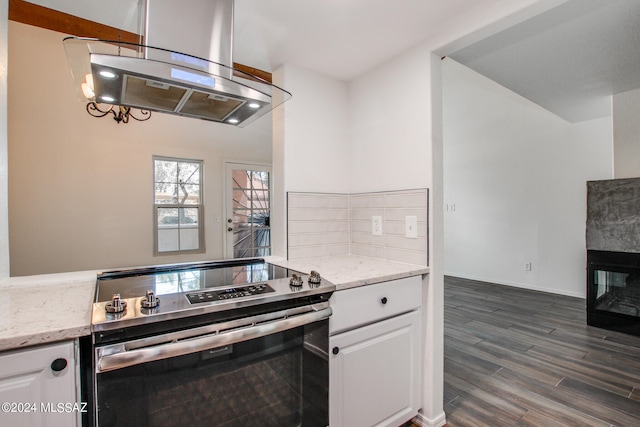 kitchen featuring stainless steel electric range oven, light stone counters, white cabinetry, dark wood-type flooring, and island range hood