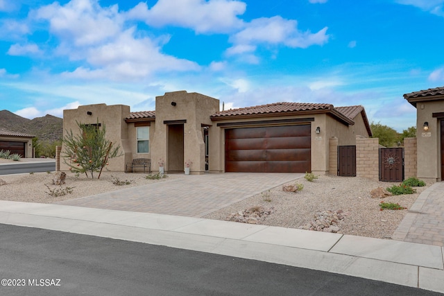 pueblo-style house featuring a garage, a gate, decorative driveway, and stucco siding