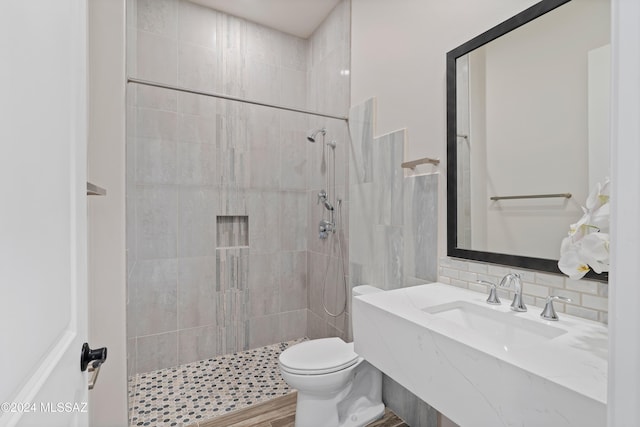 bathroom featuring hardwood / wood-style floors, backsplash, sink, toilet, and a tile shower