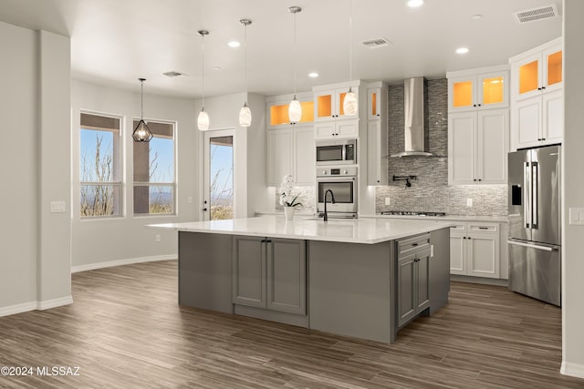 kitchen with white cabinets, wall chimney range hood, stainless steel appliances, and a large island with sink