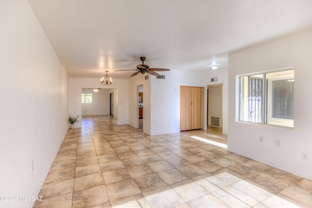 tiled empty room featuring ceiling fan with notable chandelier