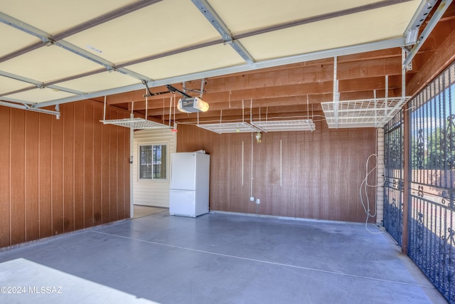 garage with a garage door opener, white fridge, and wooden walls