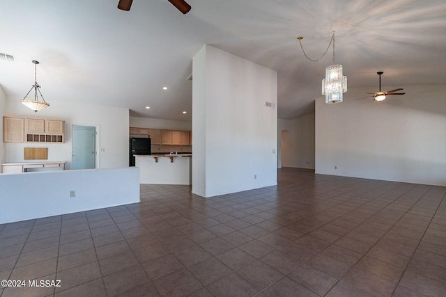 unfurnished living room featuring ceiling fan with notable chandelier and dark tile patterned flooring