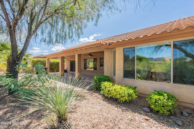 exterior space featuring a patio area, a tile roof, a ceiling fan, and stucco siding