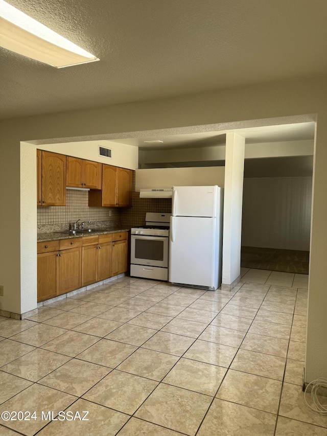 kitchen with dark countertops, visible vents, decorative backsplash, white appliances, and a sink