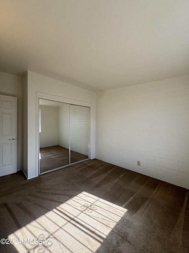 unfurnished bedroom featuring a closet, brick wall, and carpet flooring