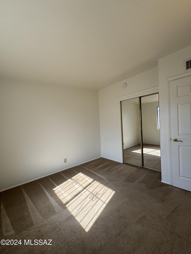 unfurnished bedroom featuring dark carpet and a closet