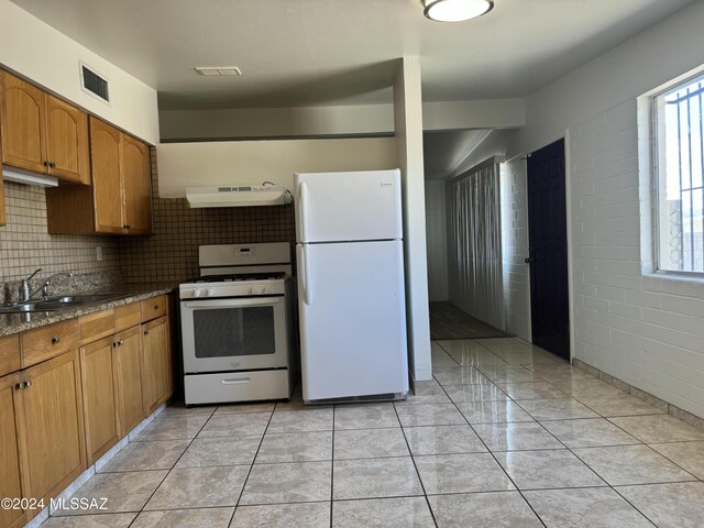 kitchen with white appliances, light tile patterned floors, dark stone counters, and sink