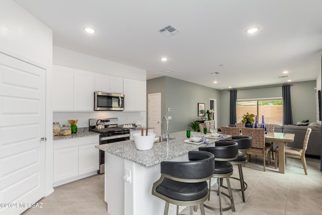 kitchen with stainless steel appliances, white cabinetry, light tile patterned floors, and light stone countertops