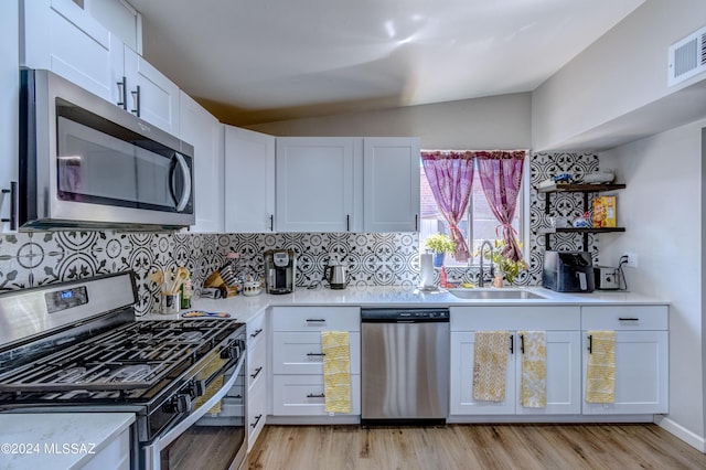 kitchen featuring sink, backsplash, vaulted ceiling, white cabinets, and appliances with stainless steel finishes