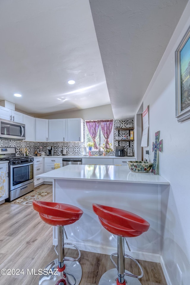 kitchen with a kitchen breakfast bar, backsplash, appliances with stainless steel finishes, white cabinets, and light countertops