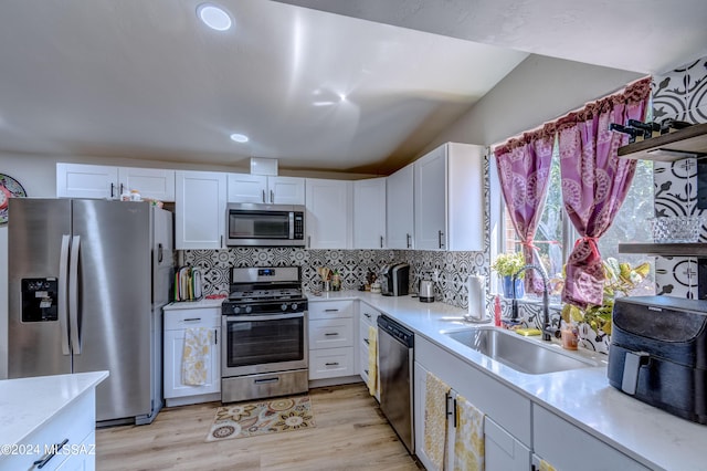 kitchen with appliances with stainless steel finishes, backsplash, sink, light hardwood / wood-style flooring, and white cabinets