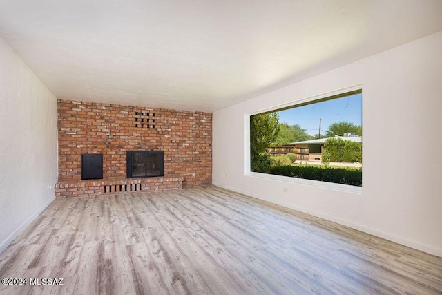 unfurnished living room featuring a brick fireplace, light hardwood / wood-style flooring, and brick wall