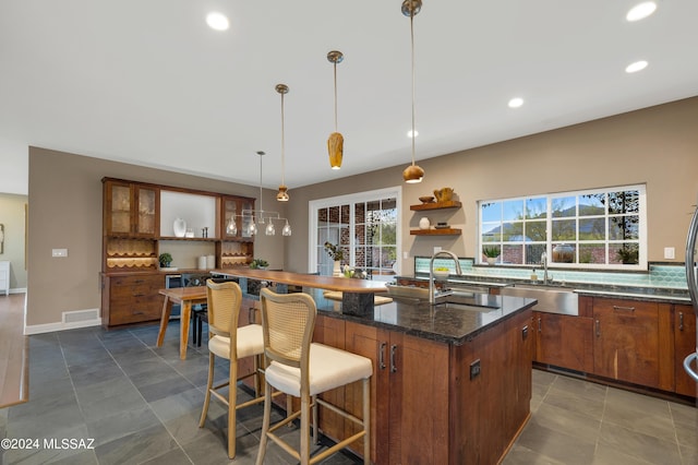 kitchen featuring a breakfast bar, decorative light fixtures, a kitchen island with sink, and sink