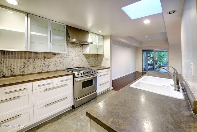 kitchen with stainless steel range with gas stovetop, backsplash, sink, white cabinetry, and wall chimney range hood