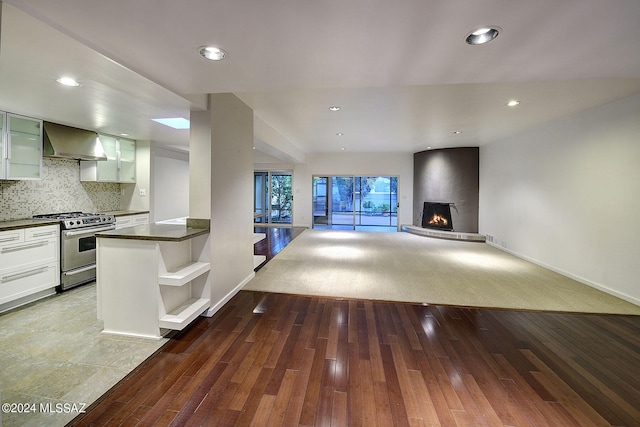 kitchen with wall chimney exhaust hood, stainless steel gas range oven, light hardwood / wood-style flooring, a large fireplace, and white cabinets