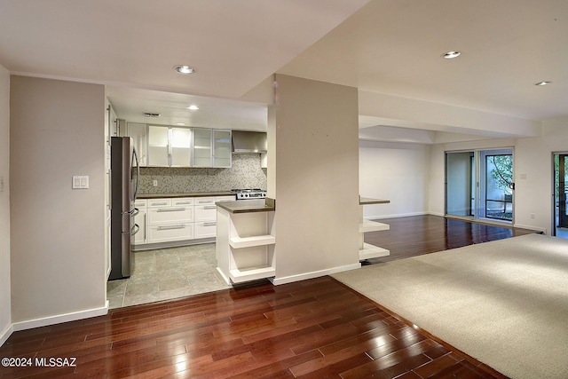 kitchen with exhaust hood, tasteful backsplash, stainless steel appliances, light wood-type flooring, and white cabinets