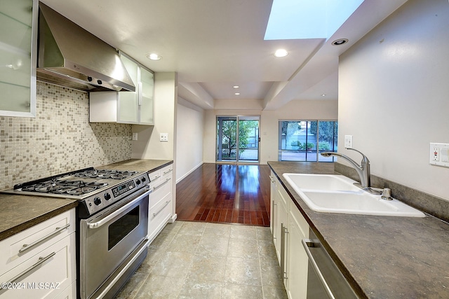 kitchen featuring wall chimney exhaust hood, appliances with stainless steel finishes, sink, white cabinetry, and a skylight