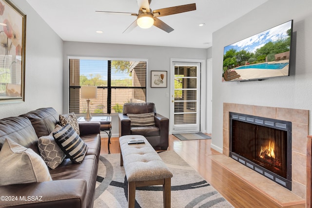 living room featuring ceiling fan, a tiled fireplace, and light hardwood / wood-style floors