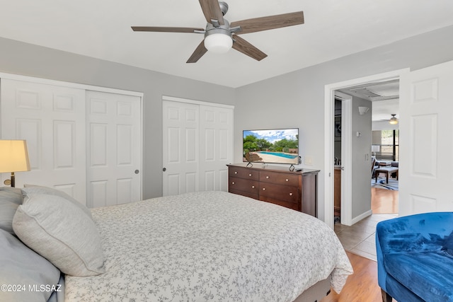 bedroom with ceiling fan, multiple closets, and light hardwood / wood-style flooring