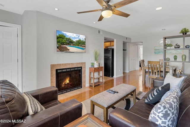 living room with light hardwood / wood-style flooring, ceiling fan, and a tile fireplace