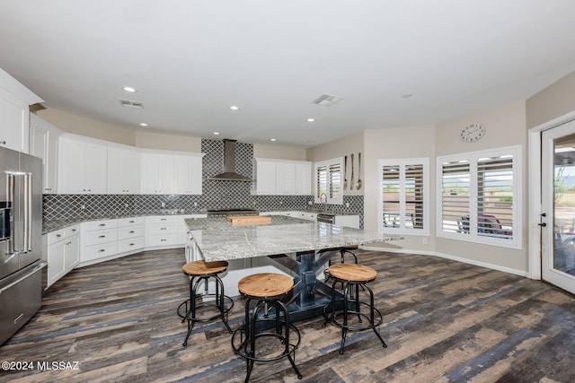 kitchen with a kitchen breakfast bar, wall chimney exhaust hood, dark hardwood / wood-style flooring, appliances with stainless steel finishes, and decorative backsplash