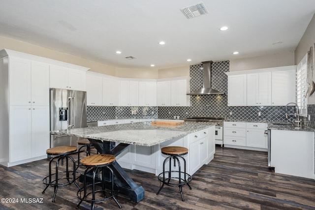 kitchen with sink, wall chimney exhaust hood, dark wood-type flooring, a kitchen island, and high quality appliances