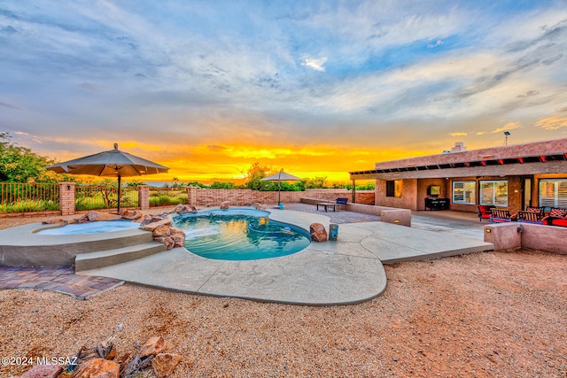 pool at dusk featuring an in ground hot tub, pool water feature, and a patio