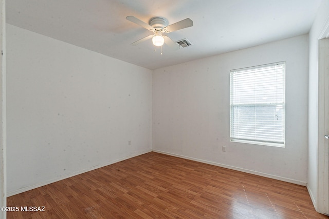 unfurnished room with a ceiling fan, visible vents, baseboards, and wood finished floors