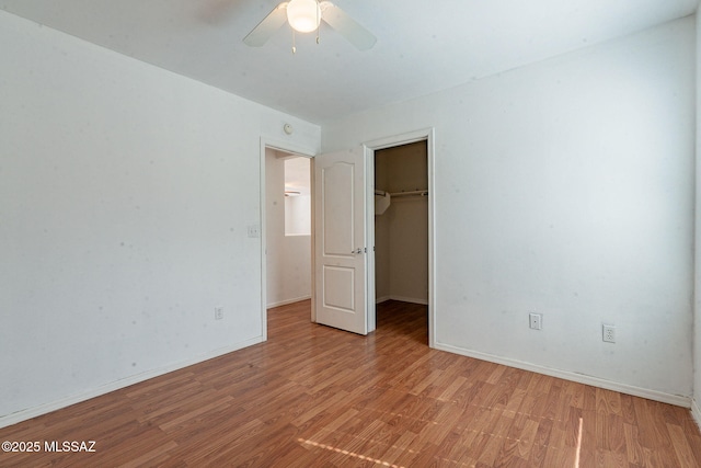 unfurnished bedroom with a closet, light wood-style flooring, a spacious closet, ceiling fan, and baseboards