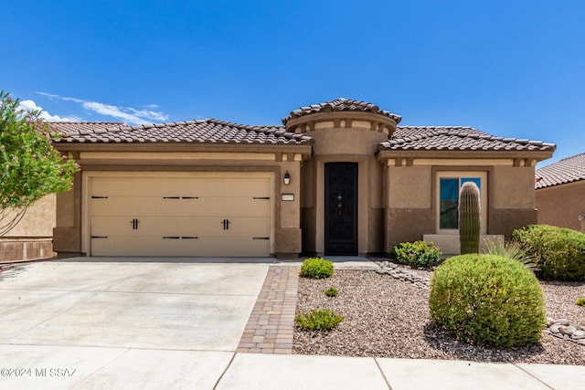 mediterranean / spanish house featuring driveway, an attached garage, a tiled roof, and stucco siding