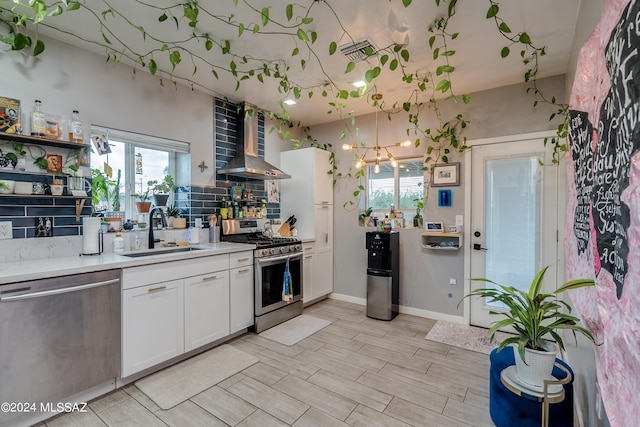 kitchen with white cabinets, stainless steel appliances, sink, wall chimney range hood, and decorative backsplash