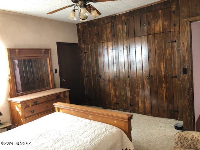 carpeted bedroom featuring ceiling fan and wooden walls