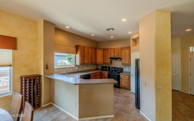 kitchen with light tile patterned floors, black appliances, kitchen peninsula, sink, and decorative backsplash