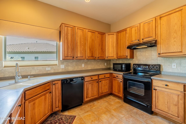 kitchen with black appliances, under cabinet range hood, backsplash, and a sink